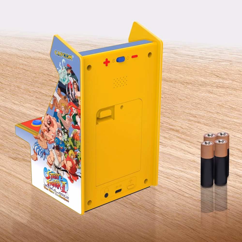 Yellow retro handheld arcade console with Street Fighter II artwork and Capcom logo on a wooden surface, with batteries nearby.